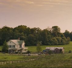 a large white house sitting in the middle of a lush green field next to a forest