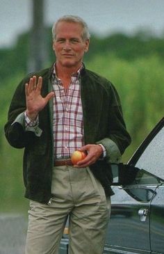 a man holding an apple standing next to a car with his hand in the air