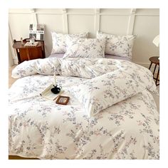 a bed with white and blue floral comforter on it's side, next to a night stand