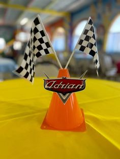 an orange cone with two checkered flags sticking out of it on top of a yellow table