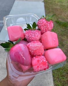 a person holding up a bowl filled with pink marshmallows and strawberries