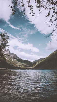 a lake surrounded by mountains under a cloudy sky