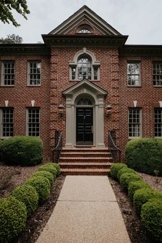 an old brick house with steps leading to the front door and two large bushes on either side