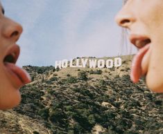 two women sticking their tongues out in front of the hollywood sign