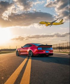 a red sports car on the road with an airplane in the sky above it and another plane flying overhead