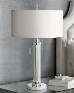 a white lamp sitting on top of a glass table next to a book and pillow