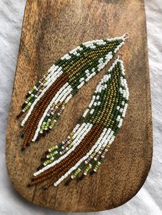 a pair of beaded earrings sitting on top of a piece of wooden plank with white and green beads hanging from it