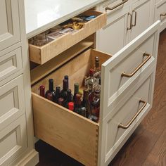 an open drawer in the middle of a kitchen with wine bottles and liquor on it