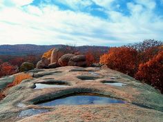 the rocks are covered in water and trees with orange leaves on them, along with blue sky