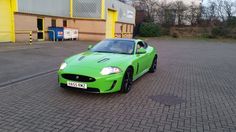 a green sports car parked in front of a yellow and brown building on a brick road