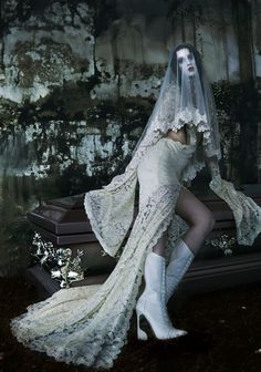 a woman in a white dress and veil sitting on a bench with her legs crossed