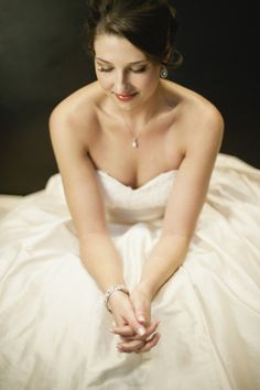 a woman sitting on top of a bed wearing a white dress and diamond bracelets