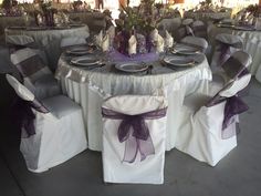 the table is set up with white chairs and purple sashes for guests to sit on