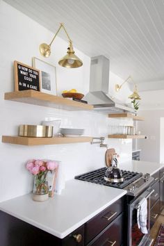 a kitchen with white counter tops and wooden shelves on the wall above stove top oven