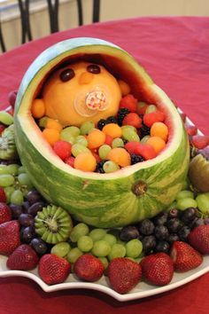 a watermelon boat filled with lots of fruit on top of a red table cloth