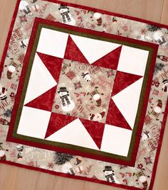 a red and white quilted table topper on a wooden floor with christmas decorations