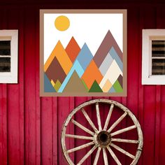 an old wagon wheel in front of a red wall with mountains on it and two windows