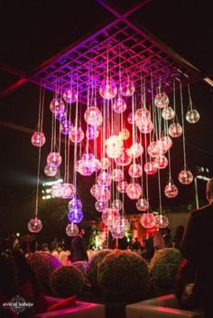 a group of people standing around a room filled with lots of hanging glass orbs