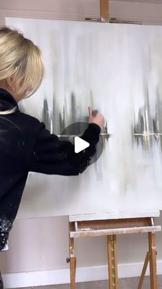 a woman is painting on an easel in front of a white board with black paint