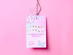 a thank you card hanging from a string on a pink background with a checkered heart