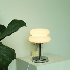 a white lamp sitting on top of a table next to a green leafy plant