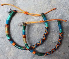 two bracelets with orange and blue beads are on a stone surface next to each other