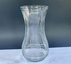 a clear glass vase sitting on top of a white tableclothed surface with a gray wall in the background