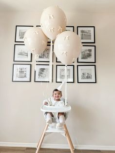 a baby sitting in a high chair with balloons hanging from it's head and legs