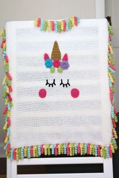 a crocheted unicorn blanket with pom poms