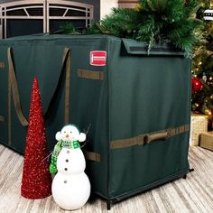 a snowman is standing next to a christmas tree in front of a storage bag