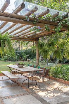 an outdoor dining table and chairs under a pergolated roof in a garden area