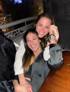 two women sitting next to each other at a table smiling and posing for the camera