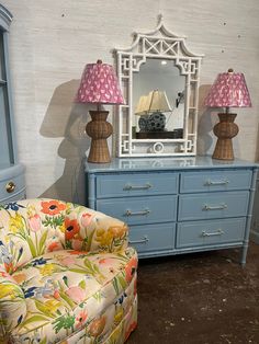 a blue dresser with two lamps on it and a chair in front of the mirror