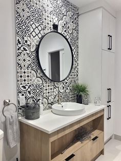 a white bathroom with black and white tiles on the wall, round mirror above the sink