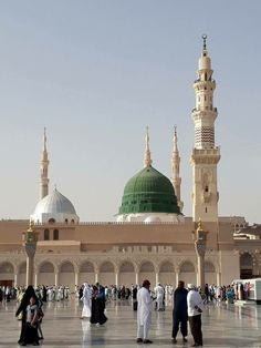 many people are walking around in front of a large building with two green and white domes