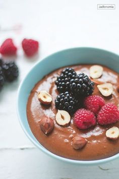 a bowl filled with chocolate pudding topped with berries and banana slices next to raspberries