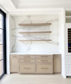 an empty room with wooden shelves and marbled wall behind the cabinets in front of a large window