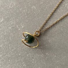 a gold necklace with a green stone in the shape of a teapot on a chain