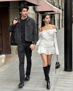 a man and woman are walking down the street holding hands while dressed in black boots