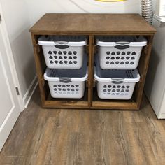 two white laundry baskets sitting on top of a wooden cabinet