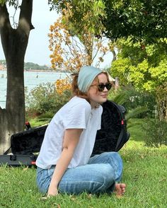 a woman sitting in the grass with an open suit case on her lap and wearing sunglasses