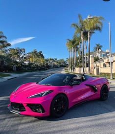 a pink sports car is parked on the side of the road in front of palm trees