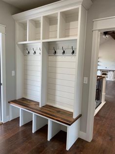 an empty room with some white benches and coat racks on the wall, along with wood flooring