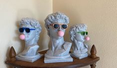 three busturines with sunglasses on top of a wooden table next to a wall