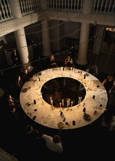 a group of people sitting around a table with candles on it in a room filled with columns