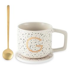 a cup and spoon sitting next to each other on a white surface with black speckles