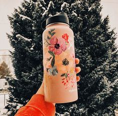 a person holding a pink water bottle in front of a snow - covered evergreen tree