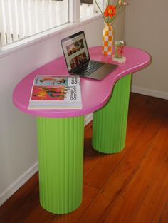 a laptop computer sitting on top of a pink table next to a vase with flowers