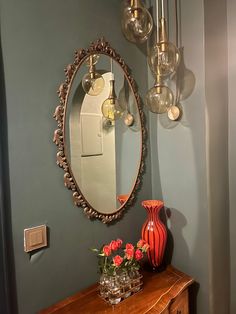 a mirror on the wall above a dresser with vases and flowers in front of it