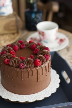 a chocolate cake with raspberries on top sitting on a tray next to a cup and saucer